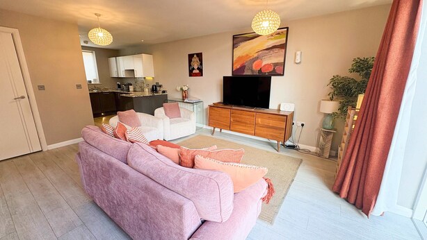 A modern living room with a sofa, a TV, a wooden cabinet, and a kitchen in the background. - Three bedroom House Next to Cabot Circus - Hopewell (Bristol)