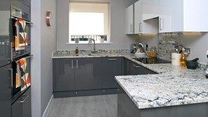 A modern kitchen with dark grey cabinets, a marble countertop, and a window with a white blind. - Three bedroom House Next to Cabot Circus - Hopewell (Bristol)
