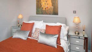 A neatly made bed with a red blanket, two bedside lamps, and a painting above it. - Three bedroom House Next to Cabot Circus - Hopewell (Bristol)