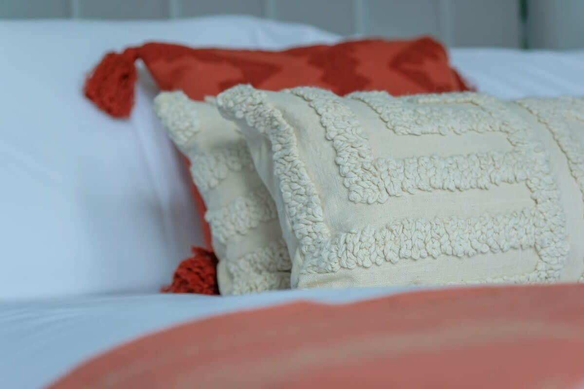 Ein Bett mit weißer und roter Bettwäsche, darunter ein weißes Kissen mit strukturierter Oberfläche und ein rotes Kissen.