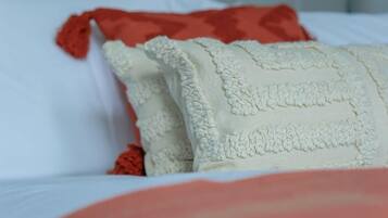 Cama com roupa de cama branca e vermelha, incluindo um travesseiro branco com padrão texturizado e um travesseiro vermelho.