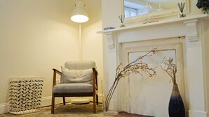 Une pièce avec une chaise, une lampe, un vase orné de branches et une cheminée.