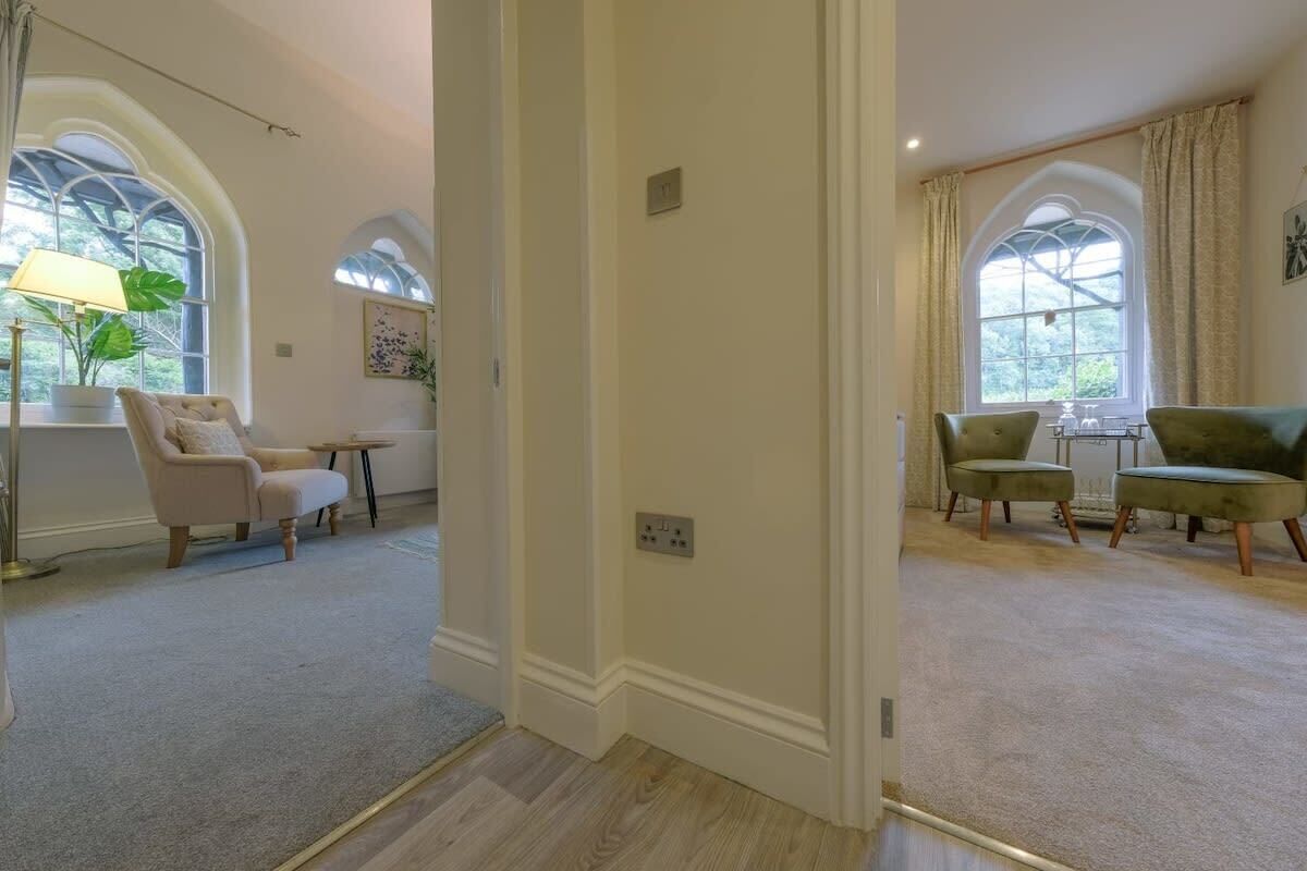 A spacious room with a large arched window, a plush armchair, a small round table, and a green sofa.