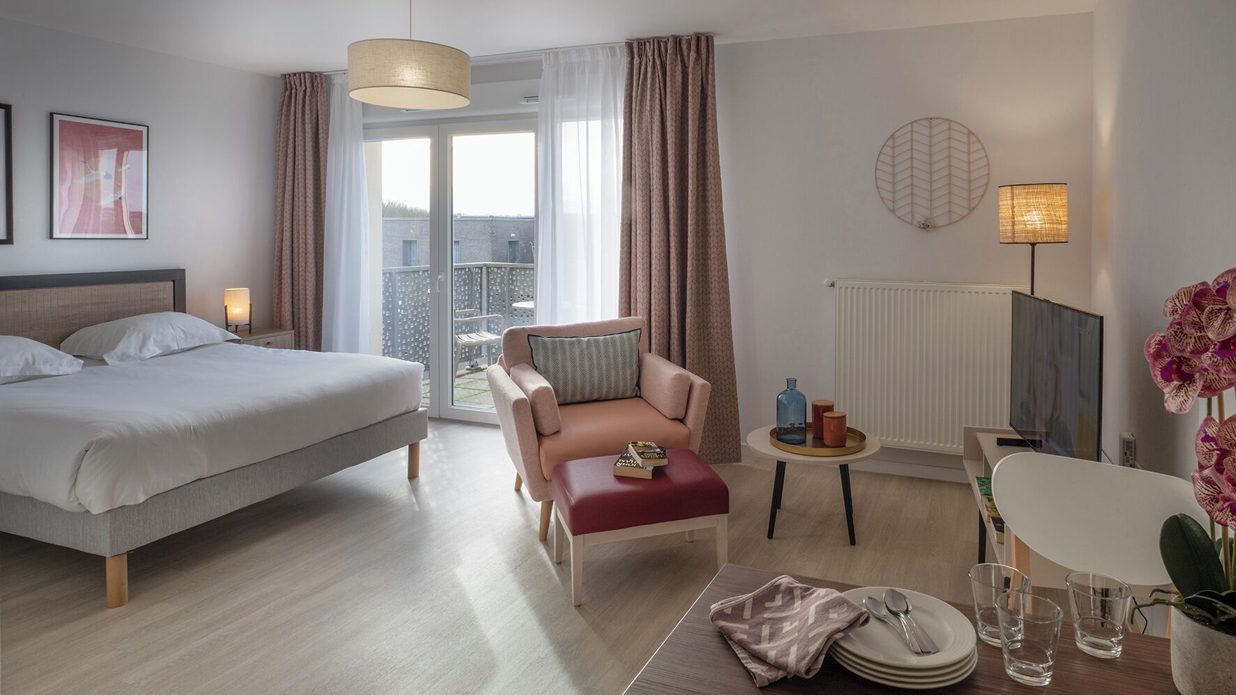 Ein modernes Hotelzimmer mit Bett, Sofa, einem kleinen Tisch, einem Sessel und Blick ins Freie.