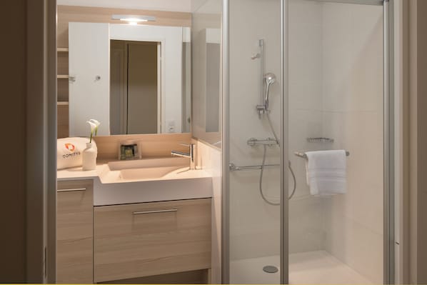 A modern bathroom with a glass-enclosed shower, a sink with a mirror, and a towel rack. - DOMITYS - La Plume de Samara (Amiens)
