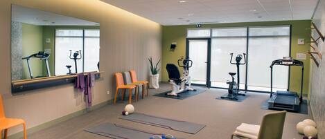 Een fitnessruimte met trainingsapparatuur, matten en stoelen.