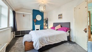 A bedroom with a bed, a dresser, a chair, a window, a door, and a wall clock. - Luckwell Cottage two bedroom (Bristol)
