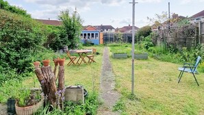 A garden with a wooden table and chairs, a path leading to a blue house, and a blue chair in the foreground. - Luckwell Cottage two bedroom (Bristol)