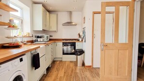A compact kitchen with a washing machine, oven, and wooden flooring. - Luckwell Cottage two bedroom (Bristol)