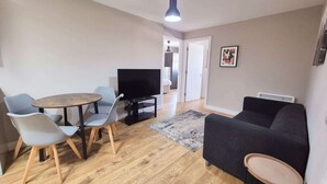 Una sala de estar con televisor, dos sillones, un sofá y una mesita.