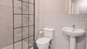 Un baño con ducha separada por vidrio, inodoro y lavamanos.