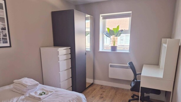 Un dormitorio con cama, escritorio, radiador y ventana con planta.