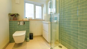 A bathroom with a toilet, a small trash bin, a window, and a shower area with glass doors.