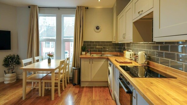 A compact kitchen with wooden countertops, a built-in washing machine, and a dining area with a table and chairs.