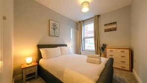 A bedroom with a bed, bedside table, dresser, and a window with curtains.