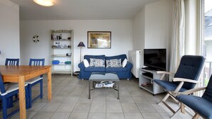 A living room with a blue sofa, wooden coffee table, and a TV. There is a bookshelf and a lamp. - Clipper 0202 Tasteful Apartment (De Haan)
