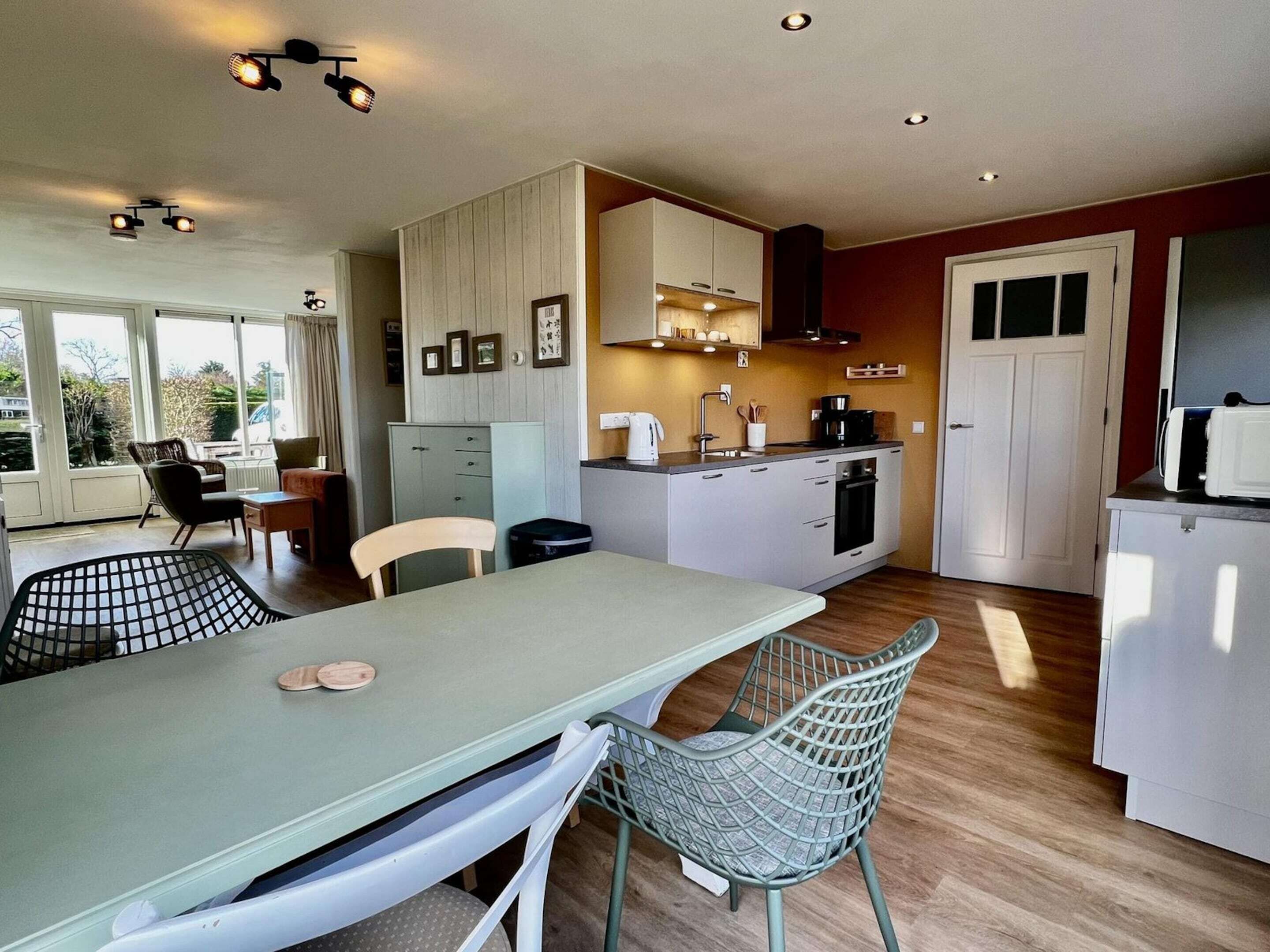 A compact kitchen with white cabinets, a dining area with a table and chairs, and a view through large windows.