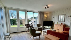A living room with a TV, sofa, chairs, and a dining table. - Modern Bungalow Close to Beach With Views (Sint Maartensvlotbrug)