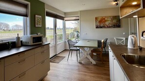 A modern kitchen with a dining area, large windows, and a view of the outdoors. - Modern Bungalow Close to Beach With Views (Sint Maartensvlotbrug)