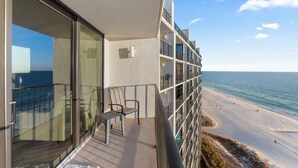 A balcony with a glass door, a chair, and a view of the beach and ocean. - Edgewater Beach Front T3 Sleeps 4 book with us now! (Panama City Beach)