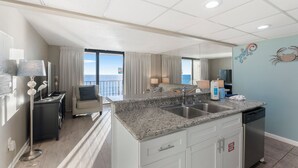 A modern kitchen with granite countertops, a built-in dishwasher, and a view of the ocean. - Edgewater Beach Front T3 Sleeps 4 book with us now! (Panama City Beach)