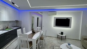 A modern living room with a dining area, a flat-screen TV mounted on the wall, and a small side table.
