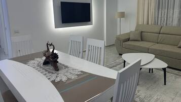 Ein modernes Wohnzimmer mit einer Couch, einem Esstisch mit Stühlen, einem an der Wand montierten Fernseher und einer Stehlampe.