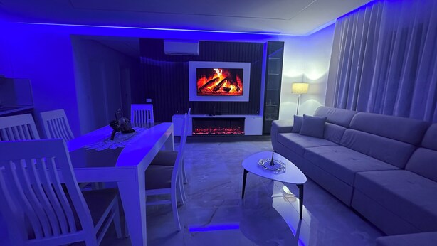 A modern living room with a flat-screen TV, a fireplace, a dining table with chairs, and a sofa.