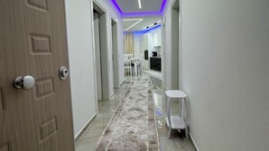 A modern hallway with a wooden door, a patterned rug, and a kitchen area in the distance.