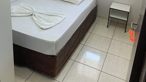Una habitación pequeña y limpia con una cama individual, una ventana con cortinas y una mesita.