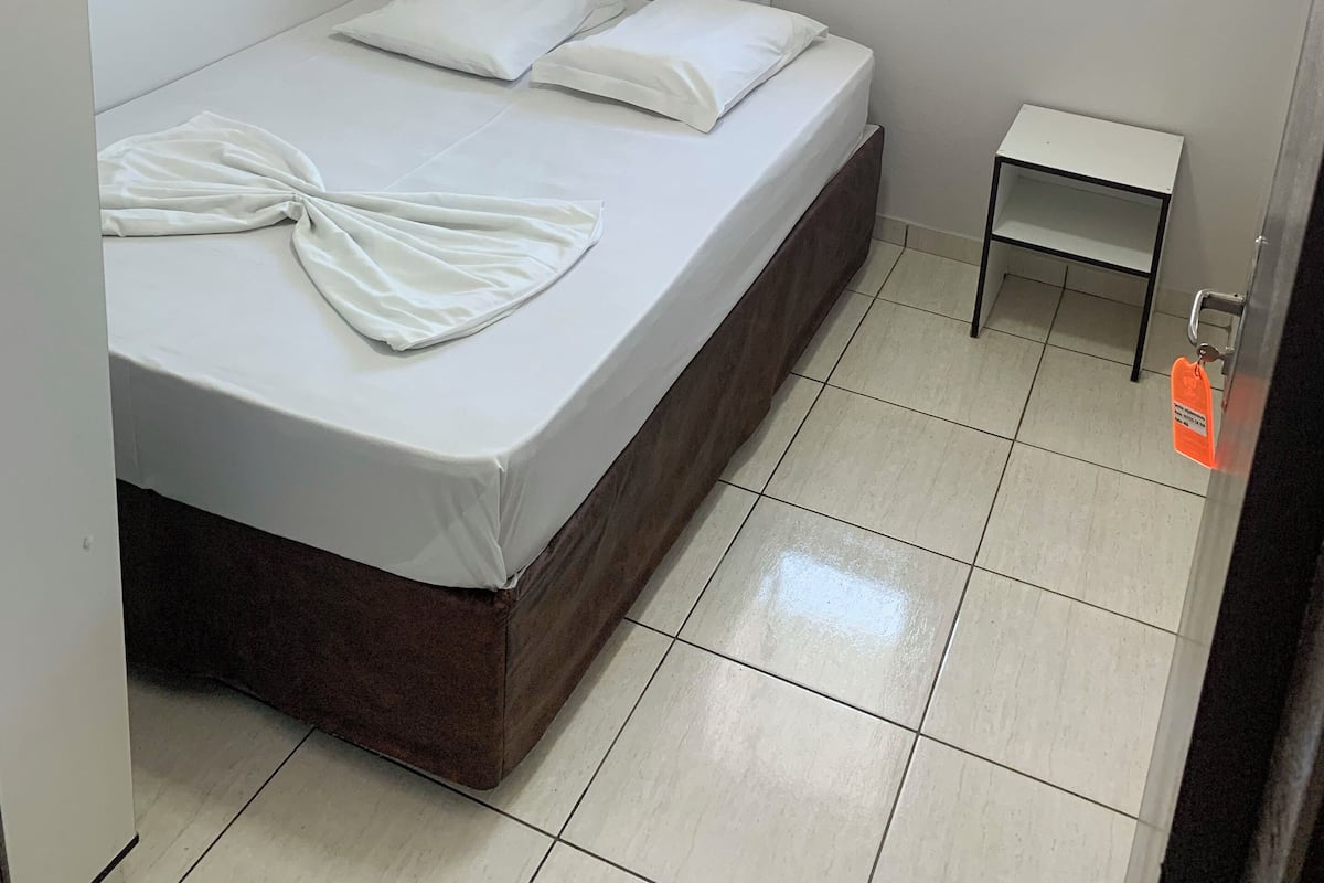 Una habitación pequeña y limpia con una cama individual, una ventana con cortinas y una mesita.