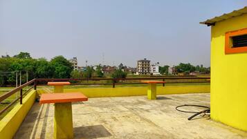 A rooftop terrace with concrete flooring, yellow and orange benches, and a yellow building with a window.