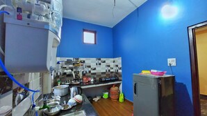 A compact kitchen with blue walls, a tiled backsplash, a sink, a stove, and a refrigerator. - Tathagata Homestay (Lumbini)