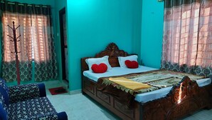 A bedroom with a wooden bed, two blue patterned chairs, and a window with patterned curtains. - Tathagata Homestay (Lumbini)