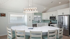 Une cuisine moderne avec des meubles blancs, un grand îlot central doté de chaises, des appareils en acier inoxydable et un luminaire suspendu.
