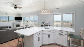 Une cuisine moderne dotée d’un grand îlot central, de meubles blancs et offrant une vue sur la plage.