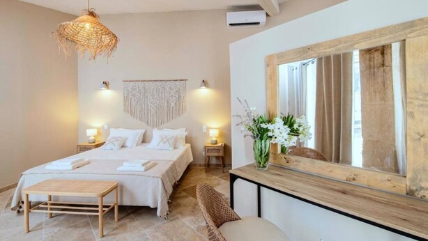 A bedroom with a bed, bedside tables, a hanging light fixture, a mirror, and a vase with flowers.