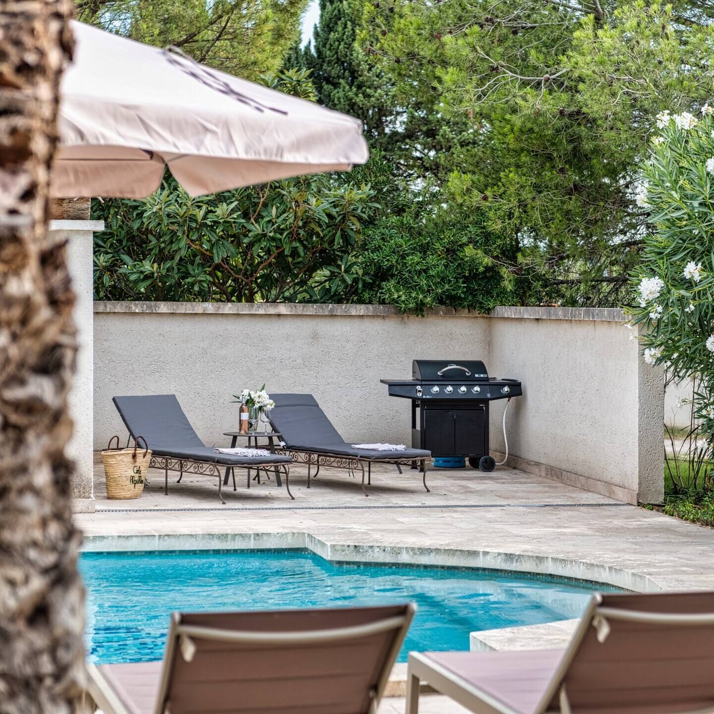 A poolside area with lounge chairs, a grill, and a small table with flowers.