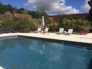 A swimming pool with clear blue water, surrounded by white lounge chairs and a pink potted plant.