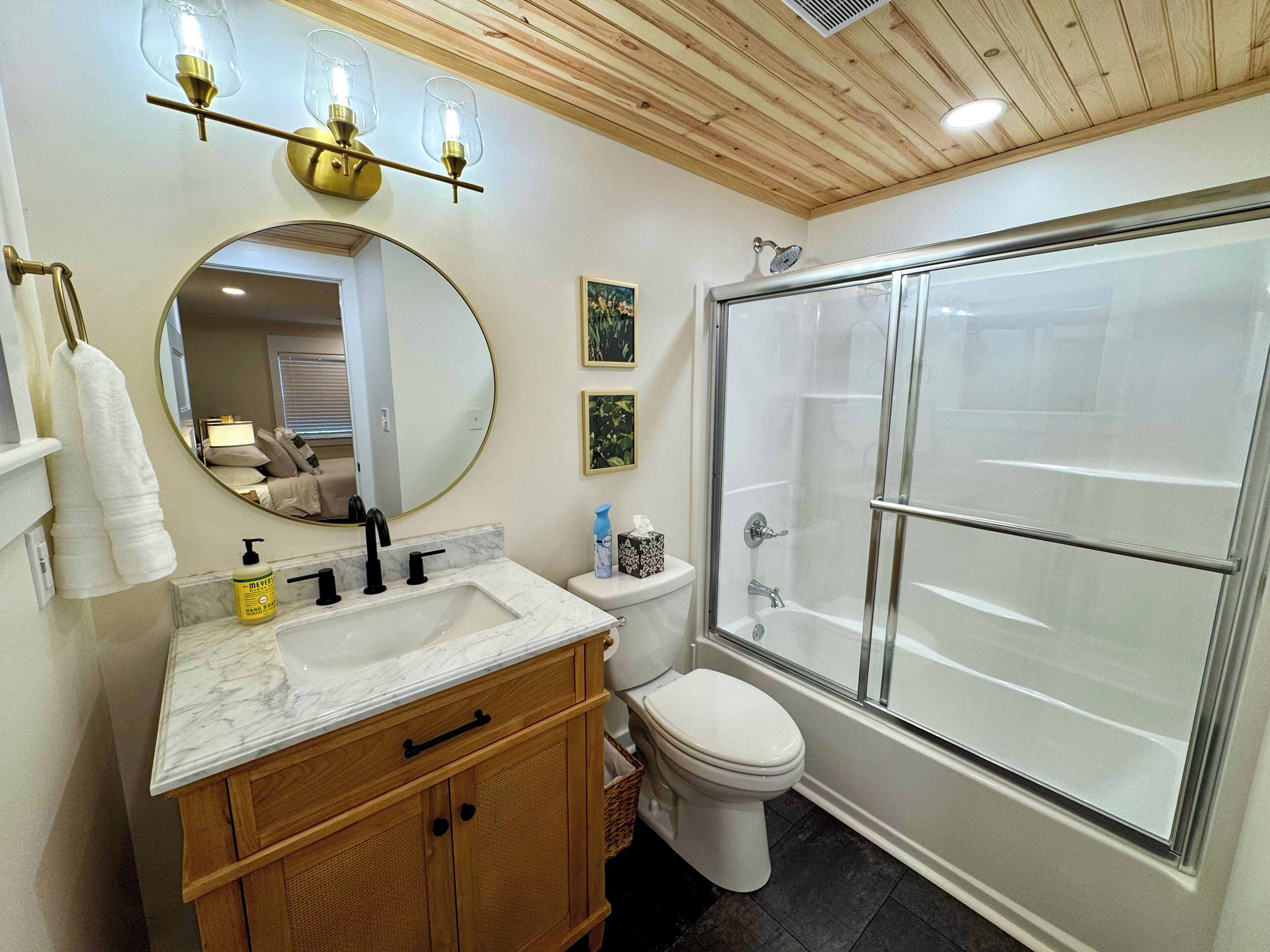 A bathroom with a marble sink, wooden vanity, a toilet, and a glass-enclosed shower.