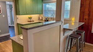 Een moderne keuken met groene kasten, een granieten aanrechtblad en een inbouw eiland met barkrukken.