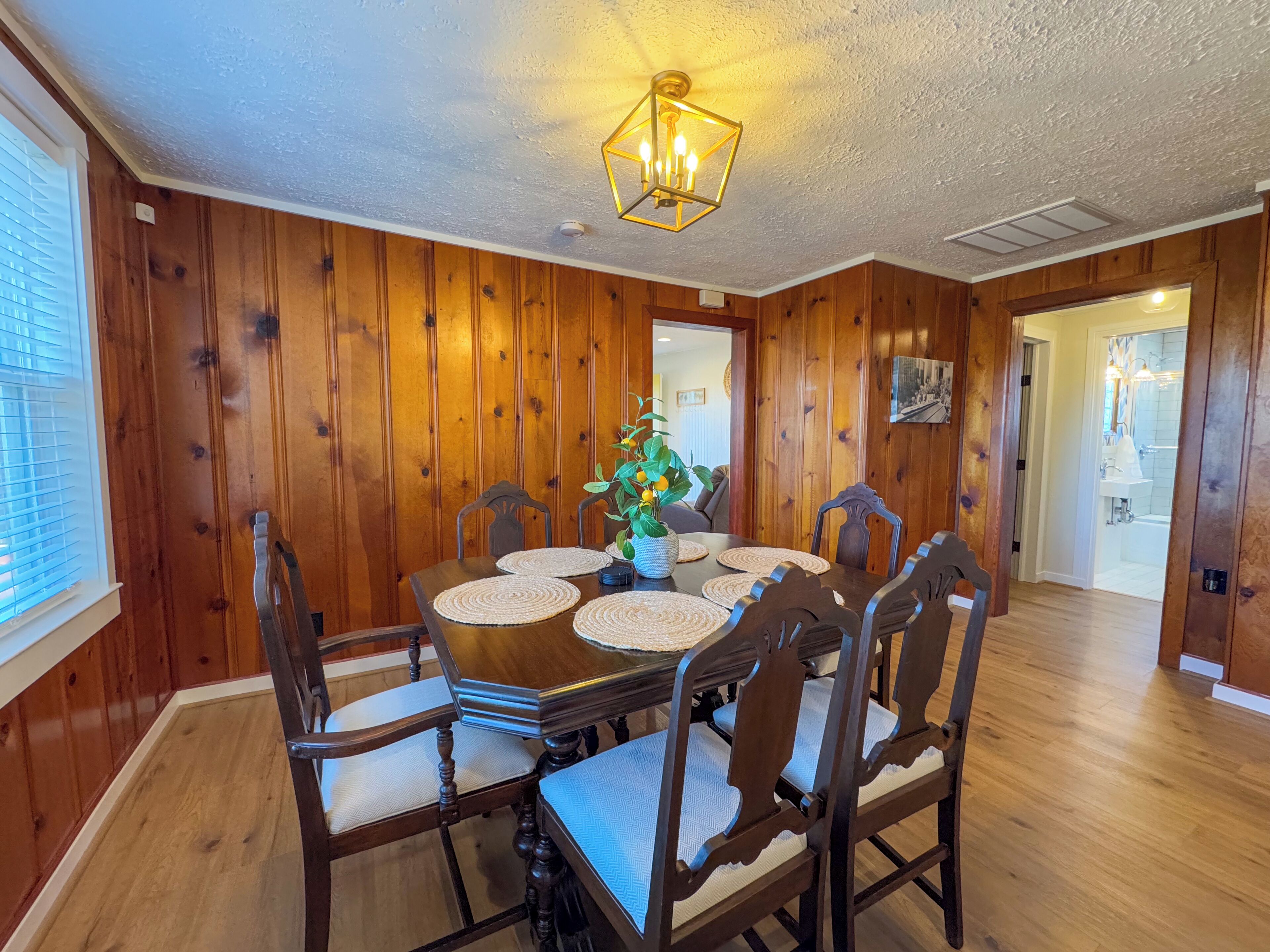 A dining room with a wooden table and chairs, a chandelier, and a view into the kitchen.