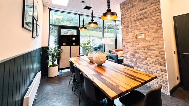 Un espacio de oficina moderno con una mesa de madera, sillas negras e iluminación colgante.