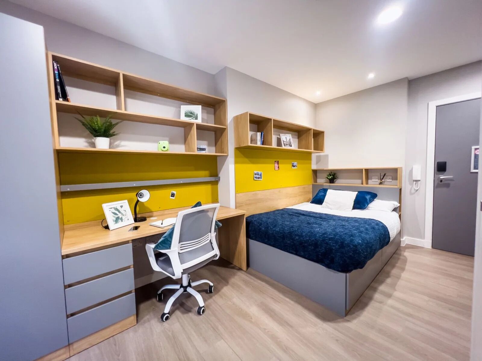 A bedroom with a bed, desk, chair, and shelving units.