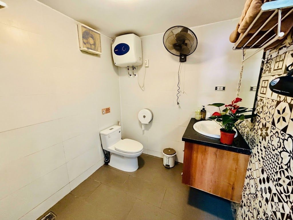 A compact bathroom with a toilet, a sink, a fan, and a small trash bin.