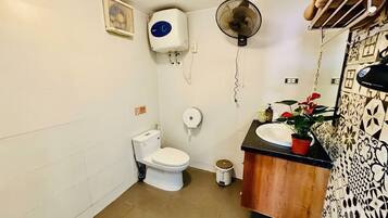 A compact bathroom with a toilet, a sink, a fan, and a small trash bin.