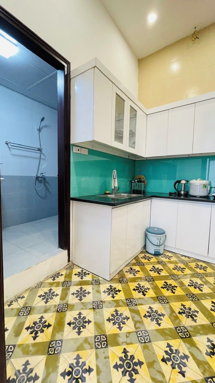 Una cocina con armarios blancos, salpicadero verde, piso estampado y una cafetera.