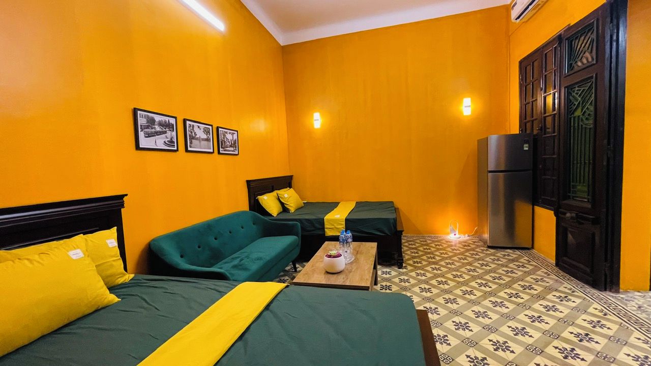 A room with two beds, a sofa, a refrigerator, and a tiled floor.