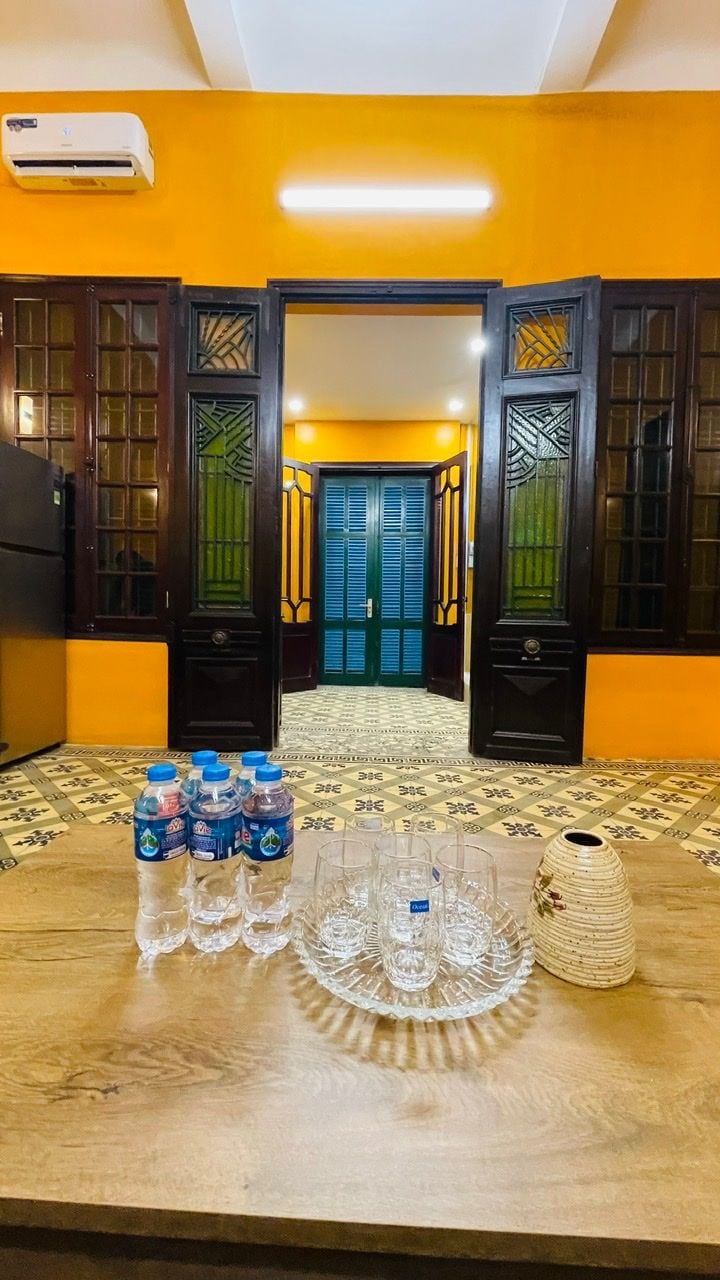 Una habitación con una pared amarilla, una mesa de madera con botellas de agua y vasos, y una puerta con paneles de vidrio decorativos.