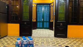 A room with a yellow wall, a wooden table with water bottles and glasses, and a door with decorative glass panels.